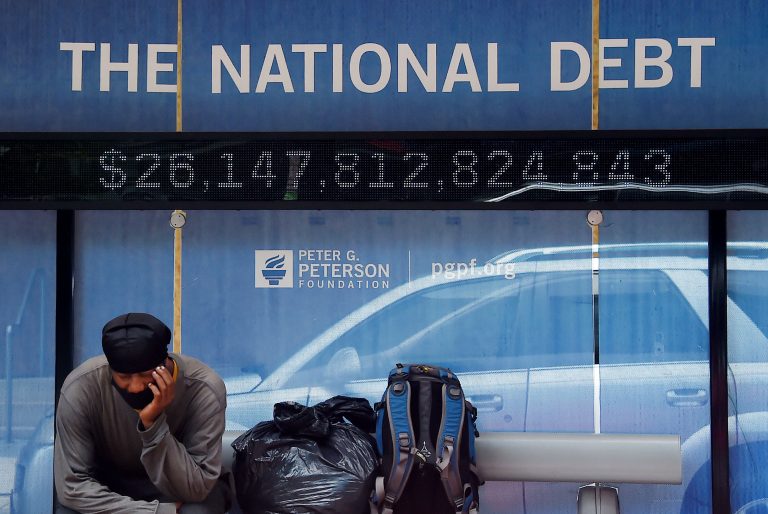 A man waits at a bus stop that displays the national debt of the United States on June 19, 2020 in Washington, DC. Senate Democrats pushed through the controversial $1.9 trillion American Rescue Plan Act of 2021 by a 50 - 49 partisan vote.