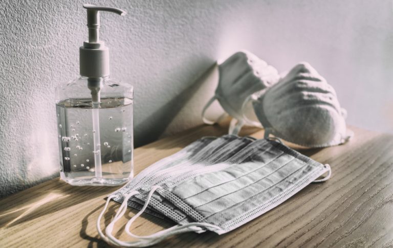Hand sanitizer sits on a counter along with 2 types of masks.