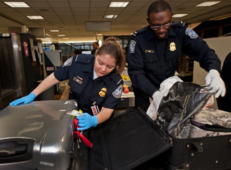 US Customs and Border Protection Officers Woo (L) and Torrey (R) open international air travelers' luggage at the US Customs and Immigration area at Dulles International Airport (IAD) December 21, 2011 in Sterling, Virgina, near Washington, DC.