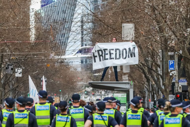 A man holds a banner reading "Freedom" atop a tram stop during an anti-lockdown protest on August 21, 2021 in Melbourne, Australia. Melbourne police under Chinese Communist Party Belt and Road signatory Premier Daniel Andrews, fired rubber bullets, tear gas, and pepper spray against citizens who have suffered more than 200 days of lockdown since the pandemic began in 2020.