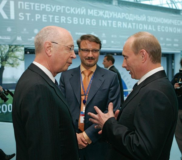 President of the World Economic Forum in Davos Klaus Schwab (L) speaks with Russian President Vladimir Putin (R) as at-the-time Russian Economic Development and Trade Minister German Gref (background) looks on in St. Petersburg on June 9, 2007. The choice of partnering with Russia’s largest bank to simulate a digital pandemic crisis is curious considering the mainstream media’s anti-Russia narrative. 