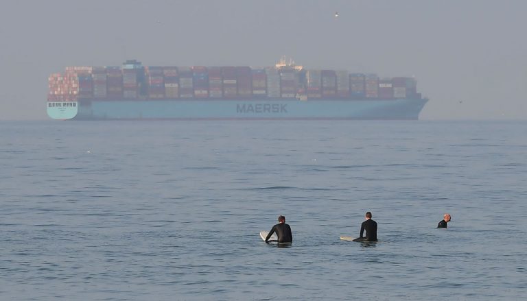 Surfers wait at Huntington Beach, California on September 25, 2021 as a container ship waits offshore. The western world is facing a major supply chain problem heading into the Christmas season that could be fueling record inflation.
