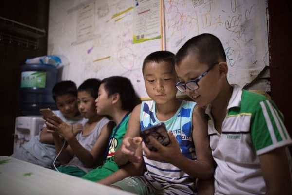In this picture taken on Aug. 17, 2017, children play smartphone games inside a room in a migrant village on the outskirts of Beijing. Surrounded by the sleek hi-tech campuses and luxury condominiums of "Beijing's Silicon Valley," migrants from the countryside recreate village life, cooking in outdoor communal areas, playing cards and showering in the street. But their community's days are numbered. 