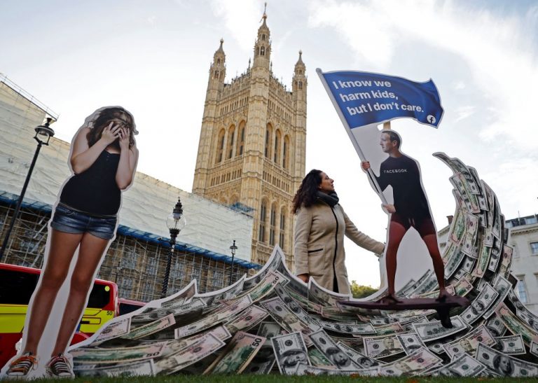 A demonstrator poses with an installation depicting Facebook founder Mark Zuckerberg surfing on a wave of cash and surrounded by distressed teenagers. It was during a protest opposite the Houses of Parliament in central London on October 25, 2021, as Facebook whistleblower Frances Haugen is set to testify to British lawmakers.