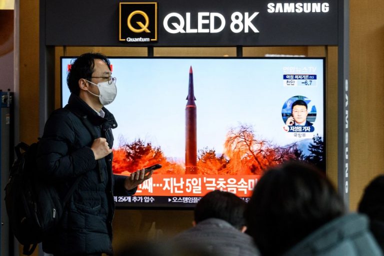 A man at a railway station in Seoul walks past a television screen showing a news broadcast with footage of a North Korean missile test on Jan. 11, 2022.