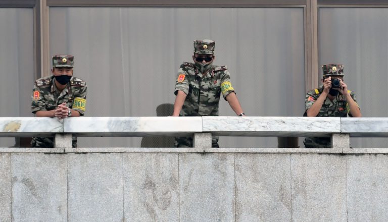 North Korean army soldiers wearing masks look at the South side of the demilitarized zone between North and South Korea.