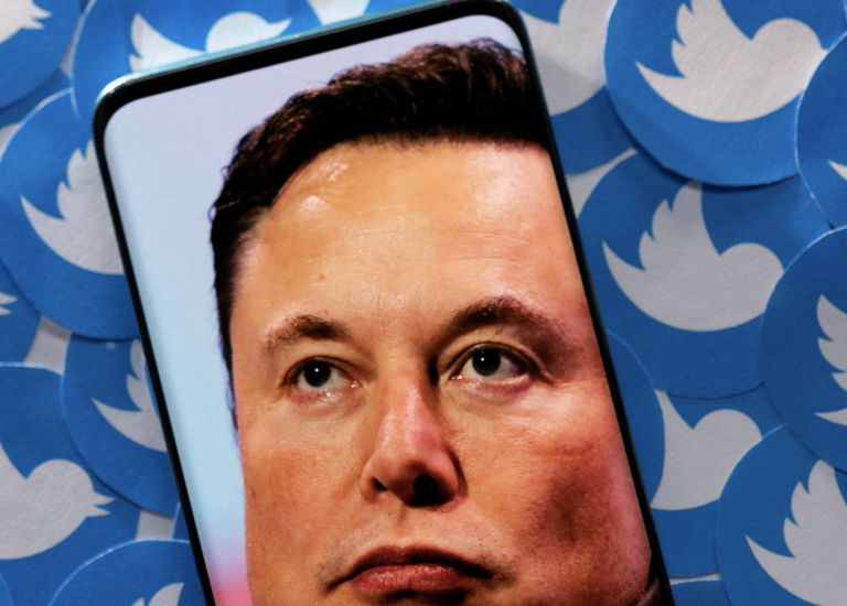 An image of Elon Musk is seen on a smartphone placed on printed Twitter logos in this picture illustration taken April 28, 2022.