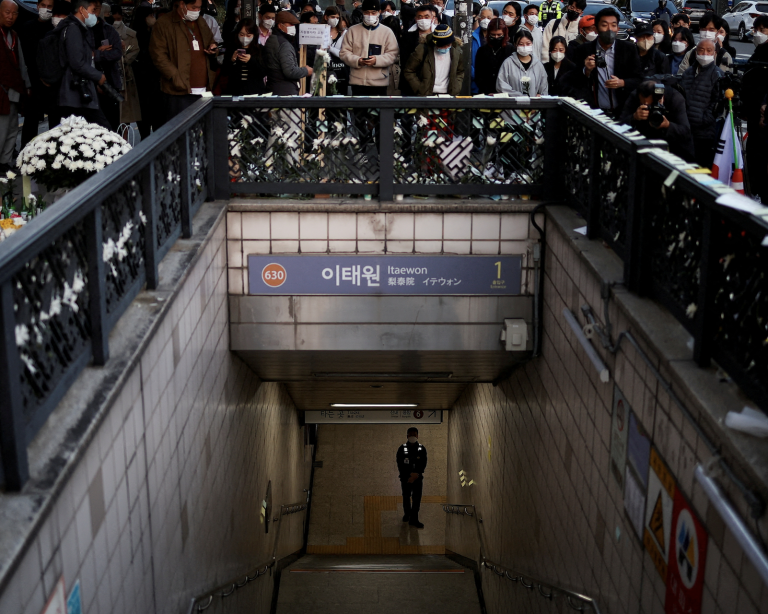 A police officer stands guard at the exit of a subway station as people gather to pay their respects following a crowd crush that happened during Halloween festivities, in Seoul, South Korea, November 1, 2022. (Image: Screenshot / REUTERS)