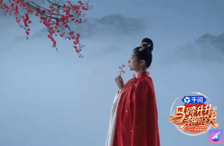 A woman in traditional Chinese attire stands in profile against a misty backdrop, holding a small branch with red blossoms, as part of a stylized performance scene from the Henan Spring Festival Gala.